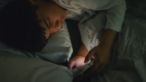 Young-Boy-In-Bedroom-At-Home-Lying-In-Bed-Using-Mobile-Phone-To-Text-Message-At-Night-5